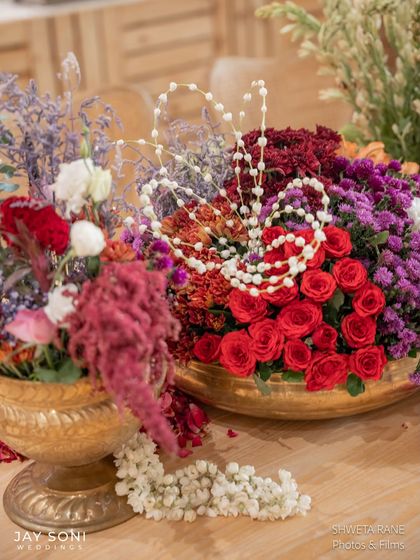 A lush centerpiece of red roses and purple fillers, adorned with strings of jasmine buds for a classic and fragrant combination.