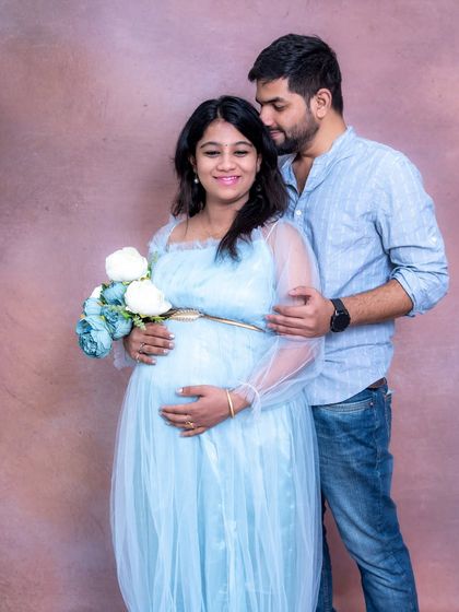A happy couple's portrait in our studio. The mom-to-be is wearing a light blue gown and holding a bouquet.