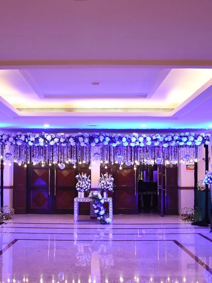 An entrance designed for a starry night theme. The doorway is adorned with hanging crystals and white florals, illuminated with cool blue and purple lights to create a celestial, shimmering effect.