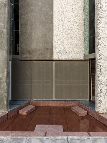 The entrance of the Artrovert studio, where contrasting material bands of rough concrete and patterned tile create a dynamic composition. A small water body adds a sensory element to the arrival experience.
