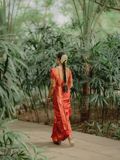 A view of the traditional South Indian braided hairstyle, beautifully decorated with flowers, walking away into a lush green background.