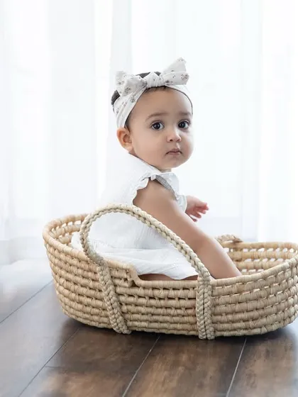 A simple and elegant portrait of a baby girl sitting in a woven basket. The natural light from the window creates a soft, beautiful glow.