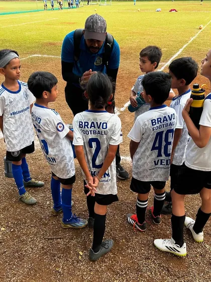 A coach huddles with his U8 team during a match, giving them encouragement and tactical advice. This shows that our greatest wins are not trophies, but the character we build in our young athletes.