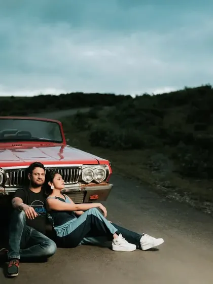 A cool, relaxed portrait of a couple sitting on the road with a vintage red convertible. This shot has a classic, romantic road trip vibe, perfect for a fun and adventurous pre-wedding theme.