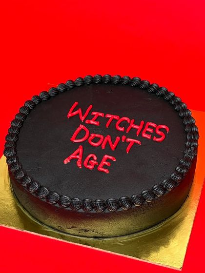 A simple statement on a classic black cake: "Witches Don't Age". This design is for anyone who defies time and stays magical. The bold red lettering on the dark frosting makes it pop.