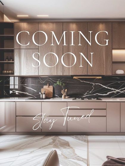 A "Coming Soon" preview of a luxurious kitchen design. The image showcases a beautiful combination of beige cabinetry, a dark marble backsplash, and warm under-cabinet lighting, promising a stylish and elegant final result.