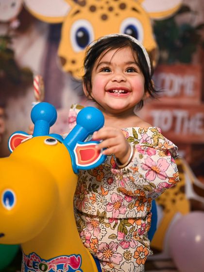 A close-up shot on the toy giraffe, capturing a bright, toothy smile. The jungle theme backdrop is visible, adding context to this happy moment.