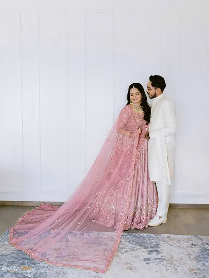 An elegant full-length portrait of the couple against a clean white wall, the bride's long, flowing veil adding a touch of drama.