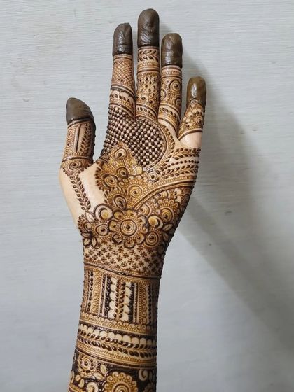 A full view of a detailed bridal henna design, extending from the fingertips to the mid-forearm. This piece combines floral patterns, checks, and bold bands for a traditional yet clean look.