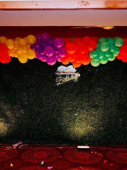This is the base we build upon for many themes. A lush green hedge wall provides a versatile backdrop, here framed by a rainbow of balloons for a Cocomelon party.