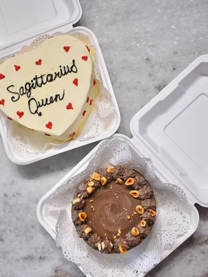 A pair of personalized bento cakes, perfect for gifting. One is a heart-shaped cake for a "Sagittarius Queen," and the other is a rich chocolate hazelnut cake.