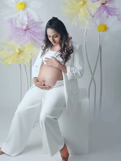 A serene and stylish shot featuring a mom to be in a white pantsuit, surrounded by delicate paper flowers. This combines modern fashion with a touch of whimsical artistry.