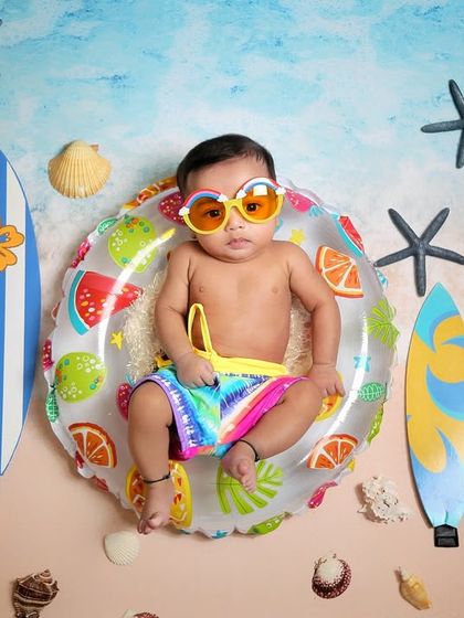 Ready to catch some waves. This beach-themed photo features a baby in a floatie with cool sunglasses, surrounded by surfboards for a fun, summery vibe.