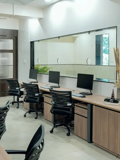 In this office design, a large internal window provides a visual connection to an adjacent area, bringing in more light. The workstations are kept clean and organized, with simple decor like dried pampas grass to add a touch of warmth.