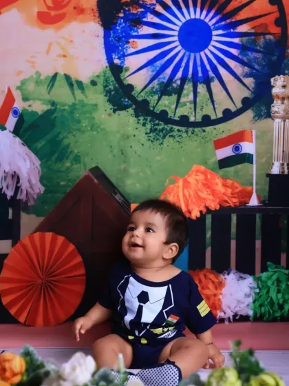 Looking up with wonder, this baby enjoys the festive atmosphere of our Independence Day studio setup, complete with tricolor pom-poms and decorations.