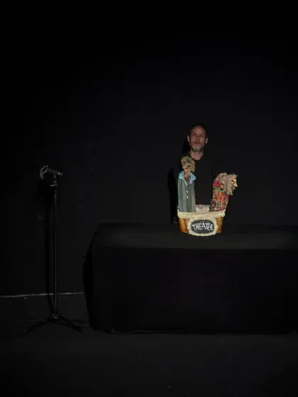 A wider view of the minimalist stage for 'Life (VIDA)'. The simple black box theatre focuses all attention on the puppeteer and the small basket of characters he brings to life.