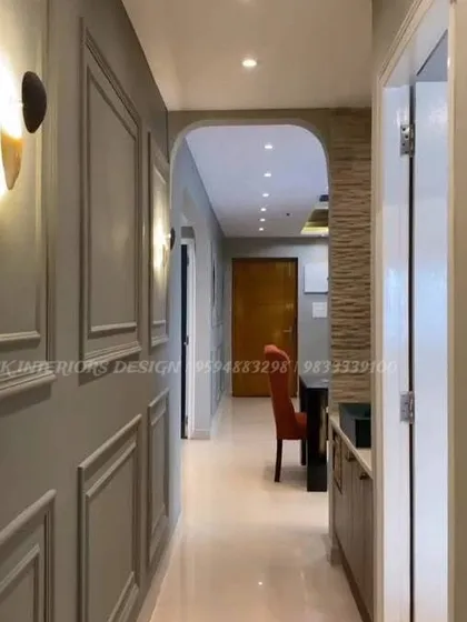 This image shows a hallway with classic grey wall moulding and modern wall sconces, leading to an arched entryway. This demonstrates how we use architectural details and lighting to enhance even transitional spaces like corridors.