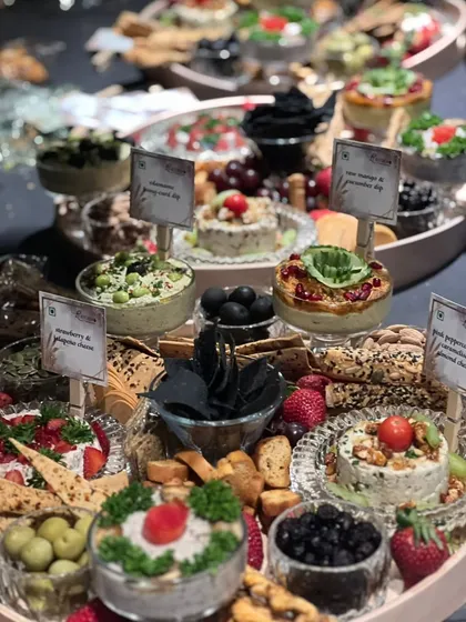 A lavish and abundant grazing table, showcasing a wide variety of cheeses, dips, crackers, and fresh fruits. Each item is clearly labeled for guests' convenience.
