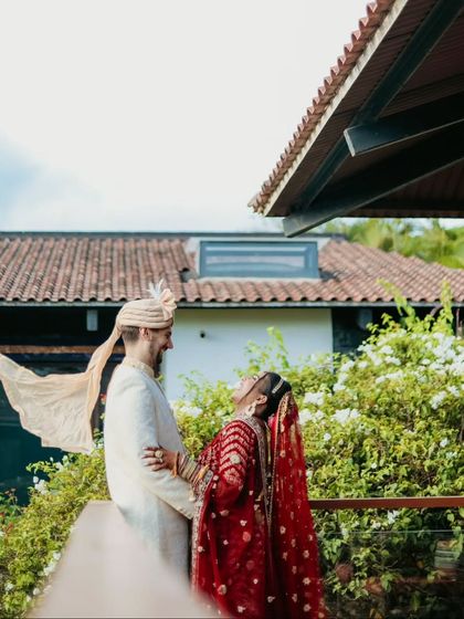 A playful, candid moment as the groom's "safa" blows in the wind, making the bride laugh.