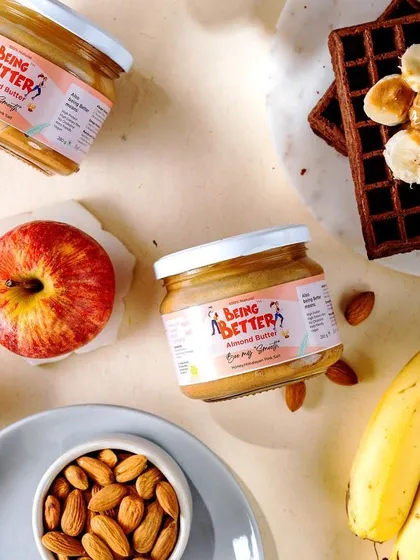 A bright and fresh flatlay of Being Better's almond butter. The composition with apples, bananas, and waffles showcases various healthy and delicious ways to use the product.