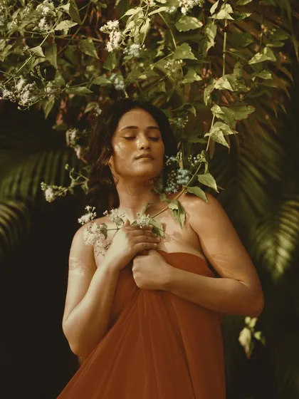 A moment of natural, raw beauty. Draped in red tulle and surrounded by foliage, the makeup is earthy and minimal, letting the natural setting and the model's serene expression shine.