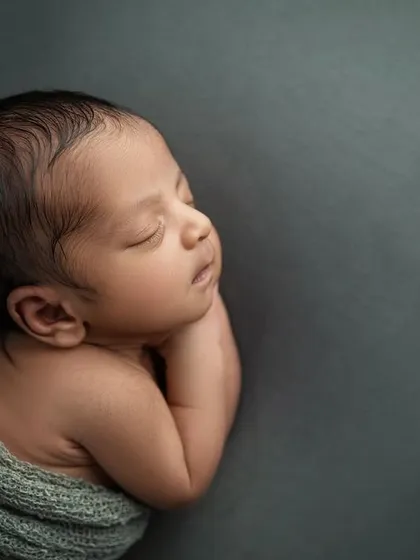 A profile view of a sleeping newborn, with soft light highlighting their features against the dark, moody backdrop.