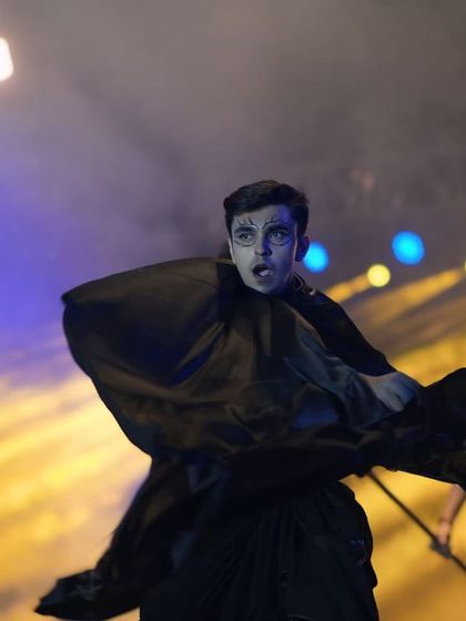 A student model in a dark, flowing costume, creating a dramatic and mysterious character on stage. This showcases the conceptual side of college fashion.