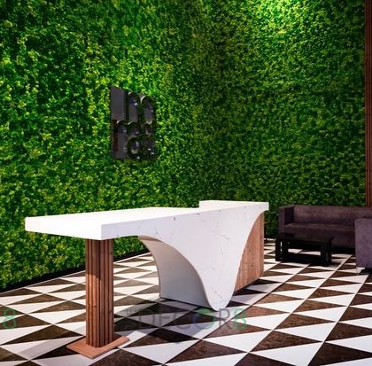 This view shows the reception desk in front of the full moss wall. The contrast between the sleek, modern desk and the natural, organic texture of the moss creates a dynamic and welcoming entryway.