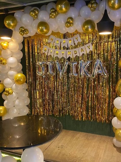 A classic gold and white second birthday party setup, with a balloon arch, shimmer backdrop, and personalized name banner.