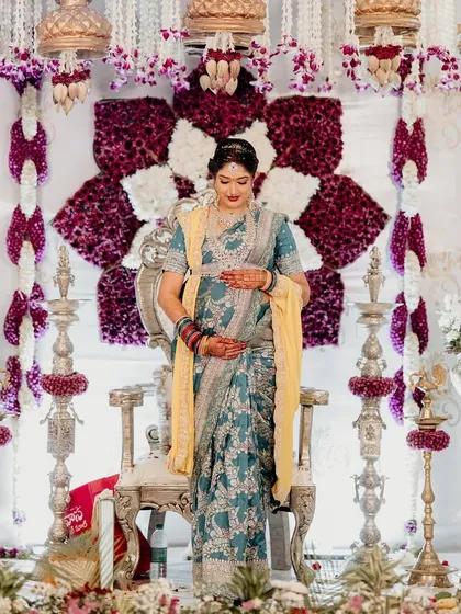 A portrait of the mother-to-be, glowing in front of a custom-designed floral backdrop. The combination of deep purple and white flowers with traditional hanging elements provides a regal and elegant setting for her special day.