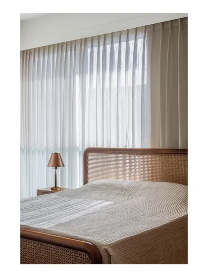 A bedroom designed to be a meditative and zen-like space. The custom bed features a caned headboard and a solid teak frame, with the entire room bathed in soft, natural light.