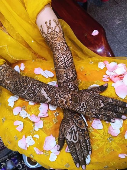 Another look at bride Aqsa's mehendi, with delicate flower petals scattered around. The design includes personalized initials on the palm.