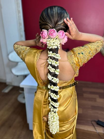 A bride adjusting her hair, showing a beautiful traditional braid with pink roses and jasmine flowers, a perfect look for a South Indian wedding.
