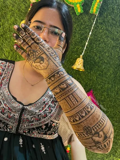 A proud bride showing off her intricate full-arm mehendi. The design is packed with details, including bands of elephants and peacocks.
