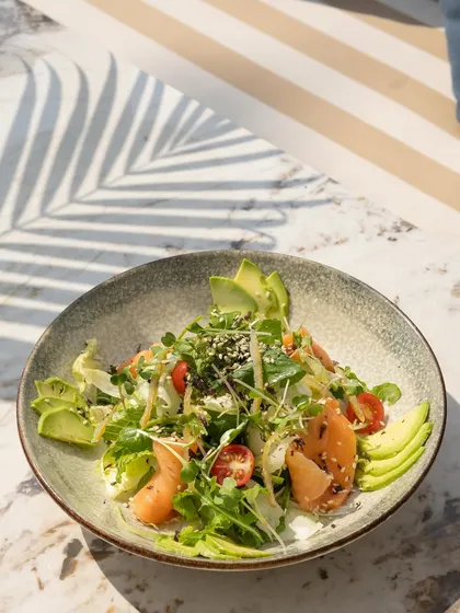 A healthy and vibrant salmon and avocado salad. The natural light highlights the freshness of the greens, the creaminess of the avocado, and the delicate texture of the salmon.