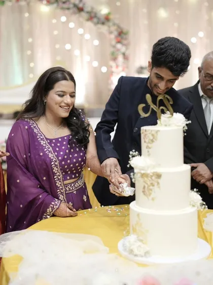 A happy client moment, capturing the couple cutting their beautiful three-tier white and gold wedding cake.