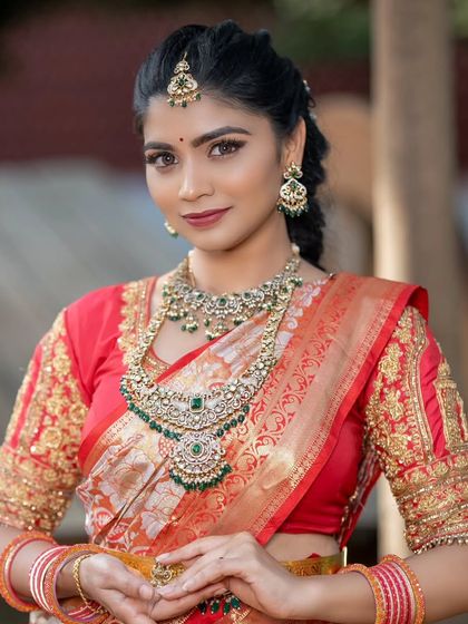 A beautiful bride wearing a Victorian-style necklace with green stones. The antique finish looks stunning against her red and orange saree.