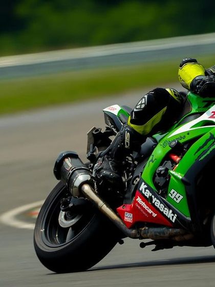 A green Kawasaki ZX-10R with full race livery leans hard into a corner, showing what a track-prepped machine can do.
