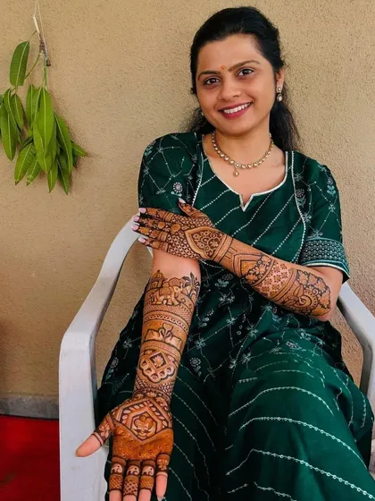 A happy client posing with her beautiful and detailed arm mehndi.
