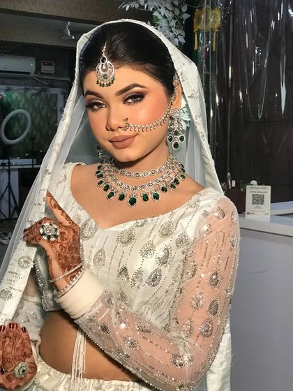 A close-up of a bride in a white sequined lehenga, paired with a stunning emerald necklace set.
