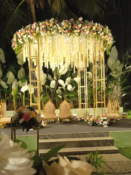 A modern mandap design with a gold metal frame and a canopy of hanging white florals, creating a chic and sophisticated look.