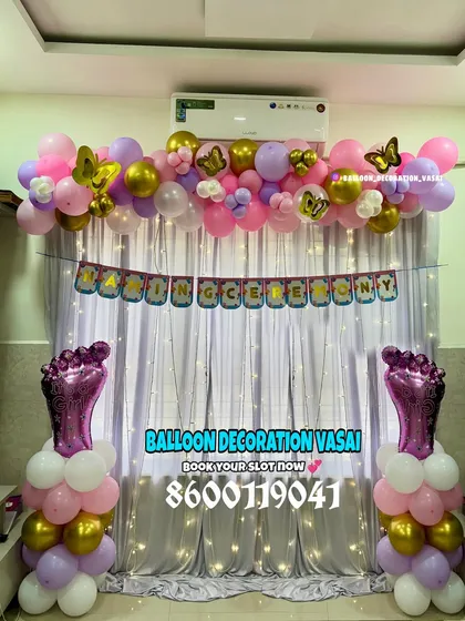 A festive naming ceremony backdrop with a "Naming Ceremony" banner and a pink, purple, and gold color scheme. The large foil baby feet on either side add a unique and charming touch.