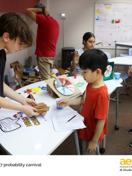 A spin of the wheel determines the next move. Middle schoolers guide elementary students through their handmade probability games, creating a fun, cross-divisional learning experience for everyone.