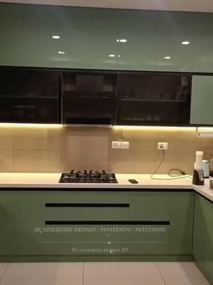 A U-shaped kitchen in a bold sage green glossy finish with black accents. The glass-fronted upper cabinets break the monotony and add a display element.