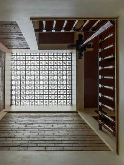 A large window with a delicate jaali pattern filters the harsh sun, casting soft, diffused light onto the brick-paved floor below. This is how we can get the daylight we need without the heat.