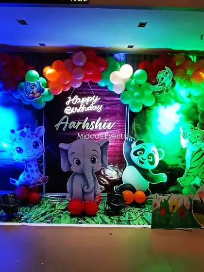 This is the full view of Aarshiv's jungle safari birthday backdrop. The setup combines a balloon arch, a custom printed background, and adorable 3D-style animal cutouts like an elephant, giraffe, and panda to create a lively scene.