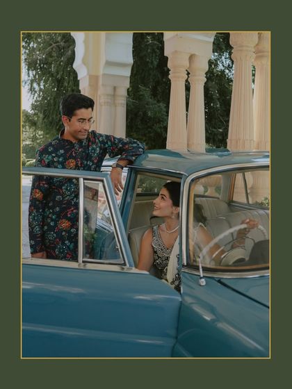 A candid moment between the couple with their vintage car in Rajasthan. The rich green border and their natural interaction create a beautiful, story-driven image.