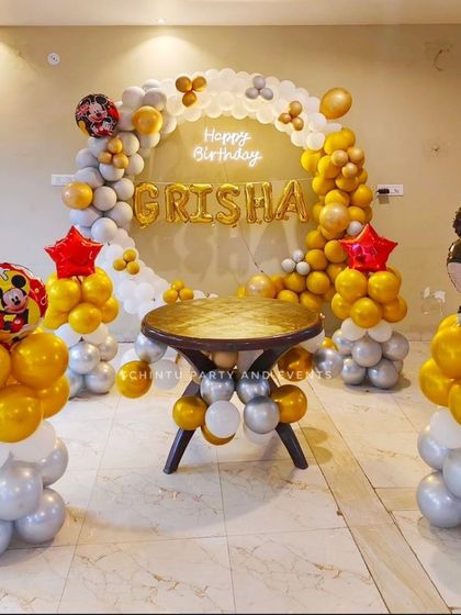 A classic Mickey Mouse themed birthday decoration. This setup uses a gold, silver, and white color scheme with a balloon ring, Mickey Mouse foil balloons, and personalized name balloons.