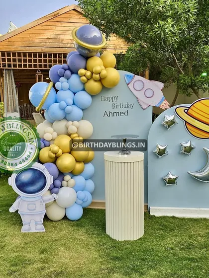 An outdoor space-themed party set up on a lush green lawn. The blue, gold, and white balloons contrast beautifully with the natural surroundings.