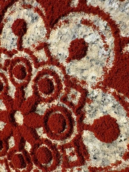 A close-up of a Rangoli pattern created with natural red powder. Rangoli is a traditional Indian art form used to bring good luck, and making the powders from natural sources makes it even more special.
